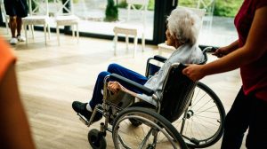 PSW worker pushing an elderly woman in a wheelchair in a long-term care home